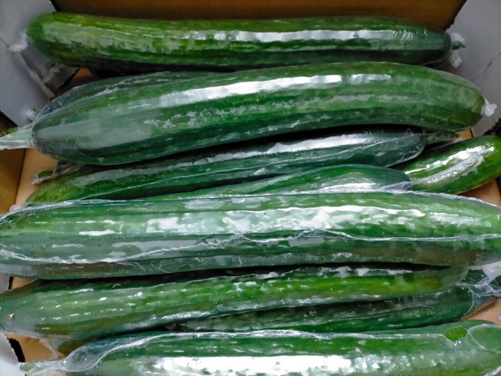 A cardboard box contains cucumbers completely wrapped in plastic. Plastic wrap used on cucumbers has been found to contain phthalates.